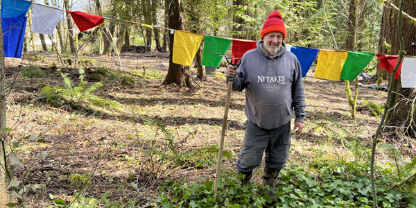 man with large rake in forest by a line of prayer flags