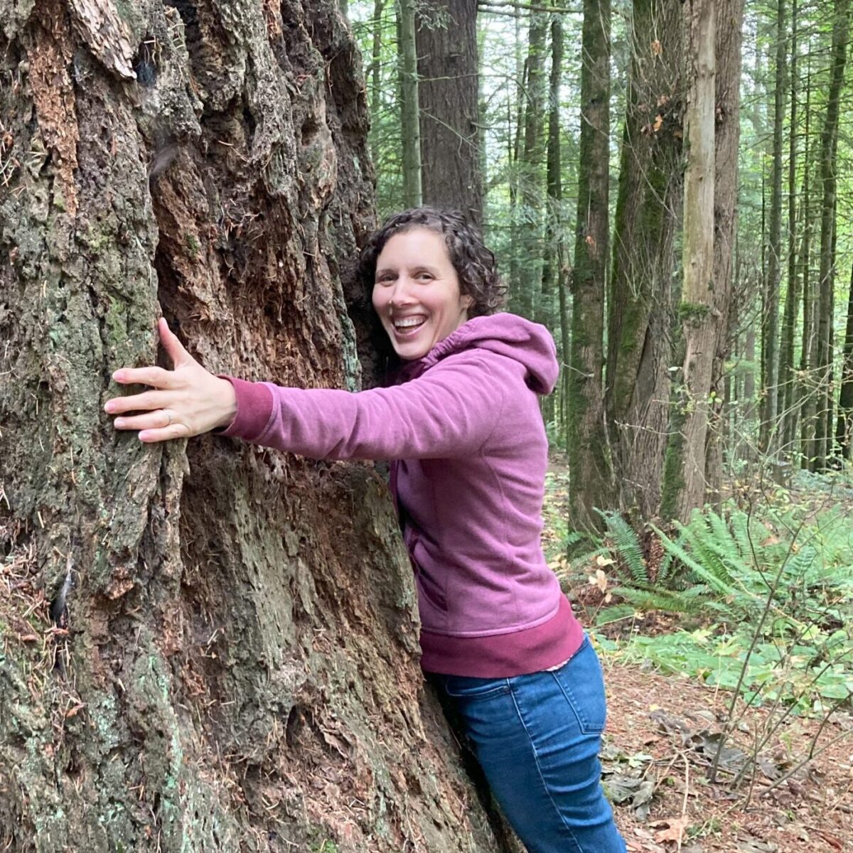 Ariana, wearing a pink sweatshirt and jeans, hugging a large tree