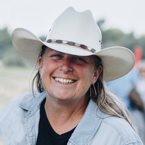 Kat, a white woman with long hair and a white cowboy hat, smiles at the camera