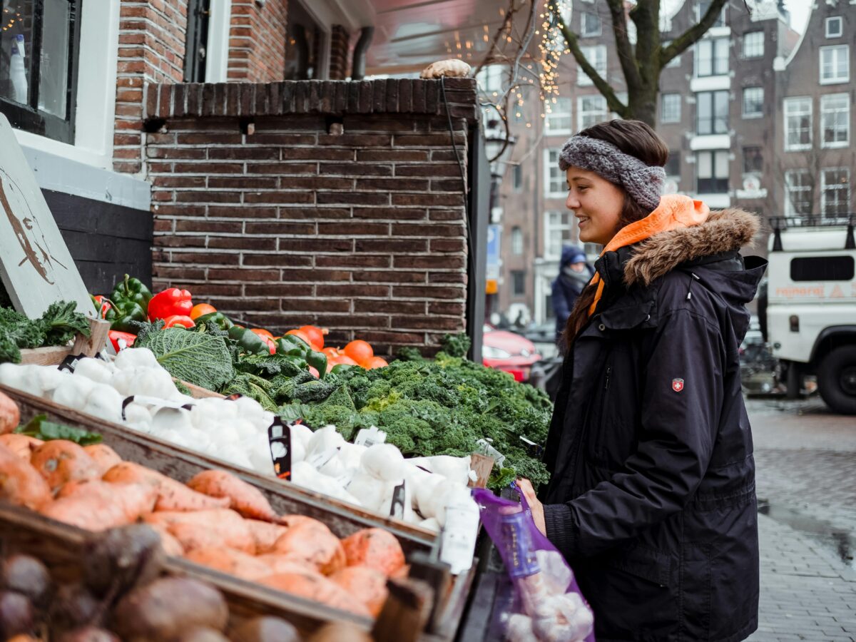 Woman with winter coat on looks at vegetables on a table, like at a farmer's market stand or shopping from Portland CSAs.