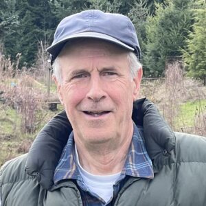 Kevin, a white man with white hair, a baseball cap, and a puffy jacket, smiles at the camera
