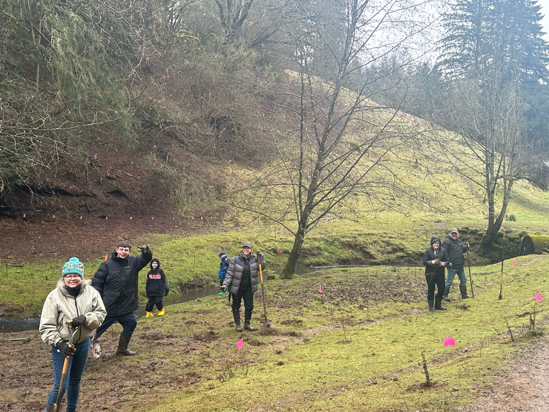 Volunteers smiling at the camera on a grassy, muddy hill on a rainy day