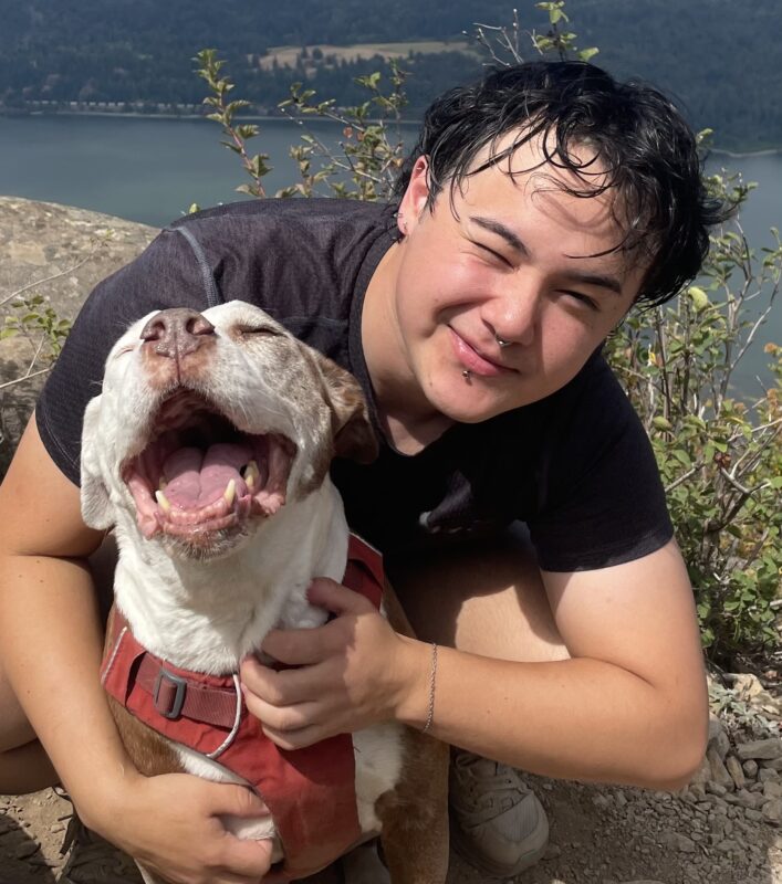 James Tracy 2025 James has short dark hair and a black t shirt. He leans and squints at the camera while posing with a large white dog
