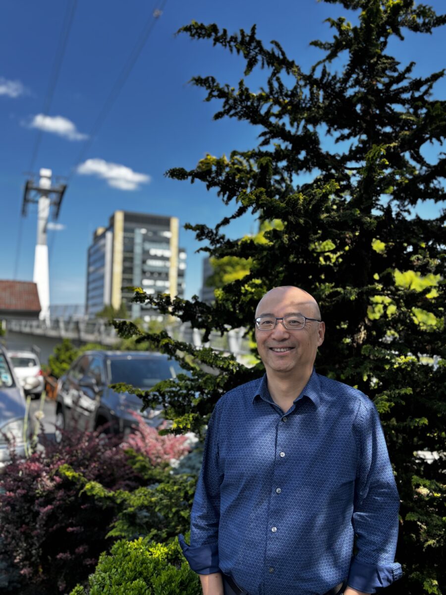 Sherman, a bald man in a blue shirt stands in front of a tree and the SW Portland skyline