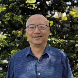Sherman, a bald man with glasses and a blue shirt, smiles at the camera