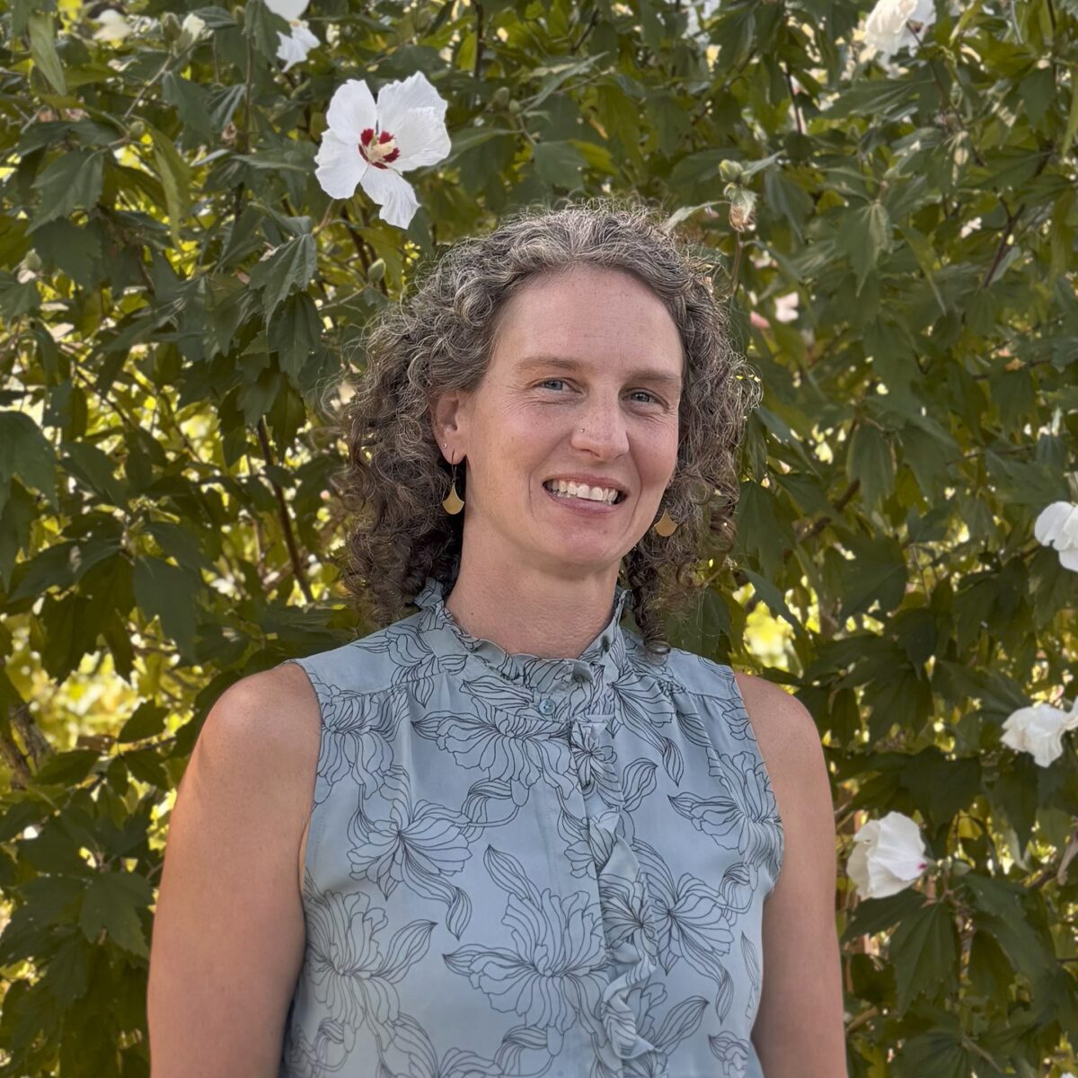 Casey, a white woman with curly gray hair, smiles and is wearing a blue floral shirt.