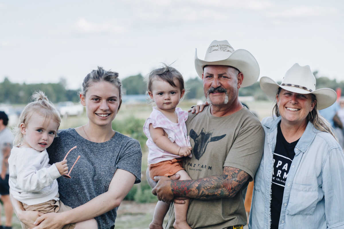 A family smiles at the camera, with two young girls, a young woman, and an older couple wears cowboy hats.