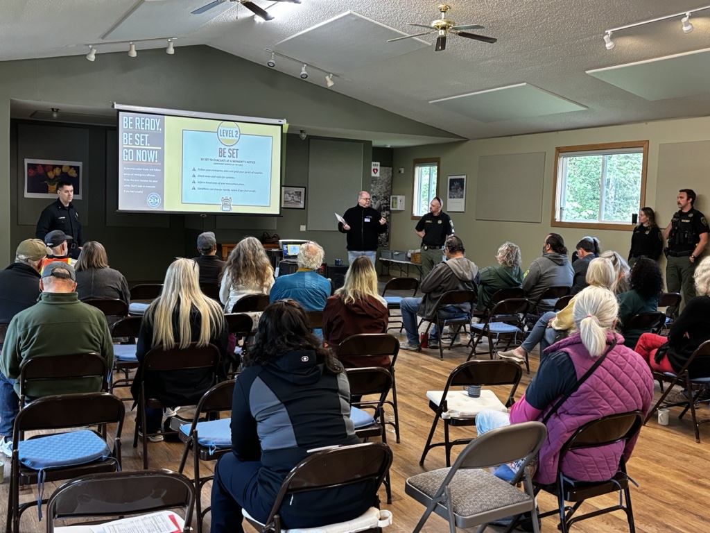 A large group of people sits in a hall, facing people who are making a presentation about emergency preparedness.