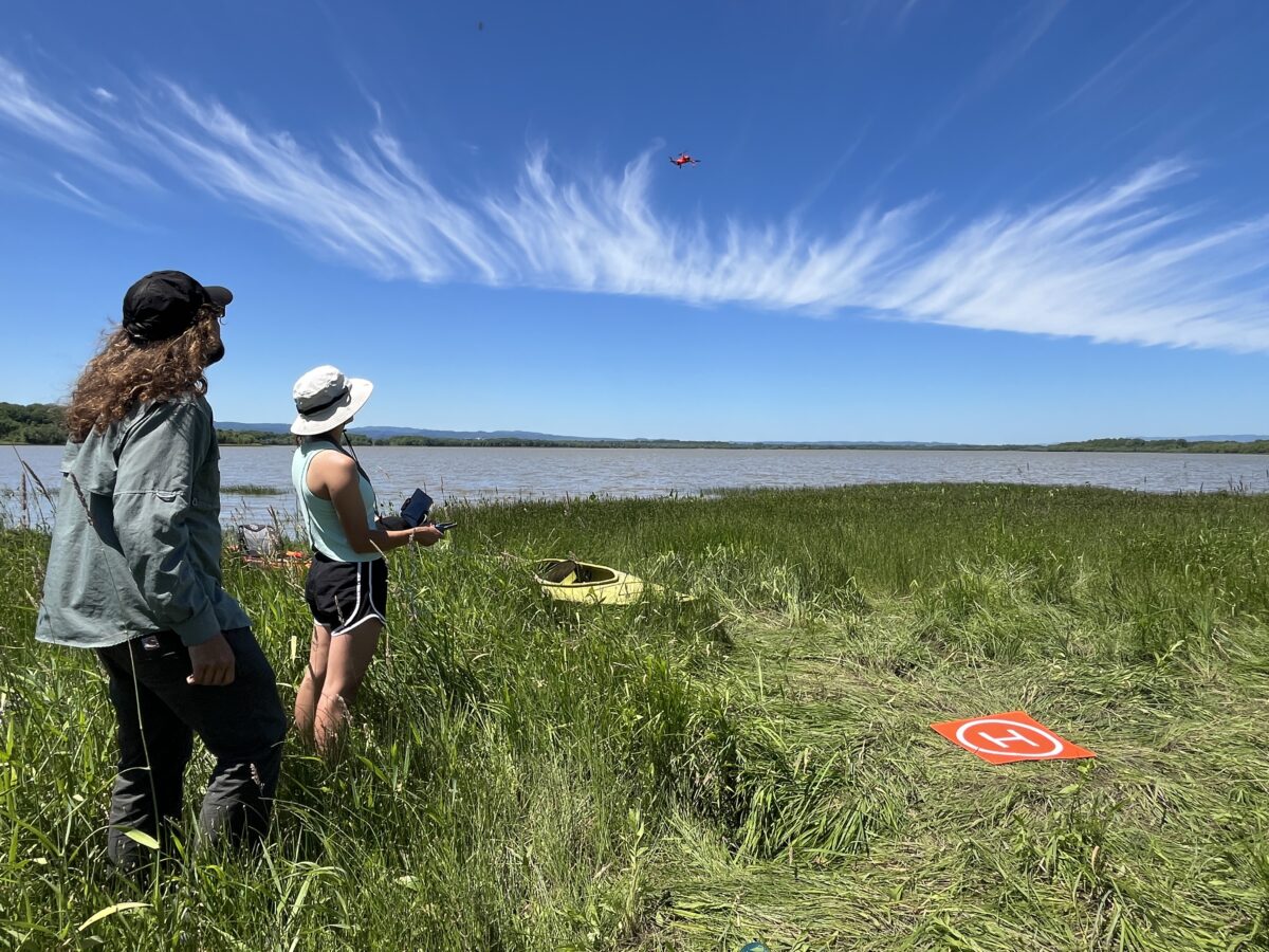 two people looking at and flying a drone over a lake