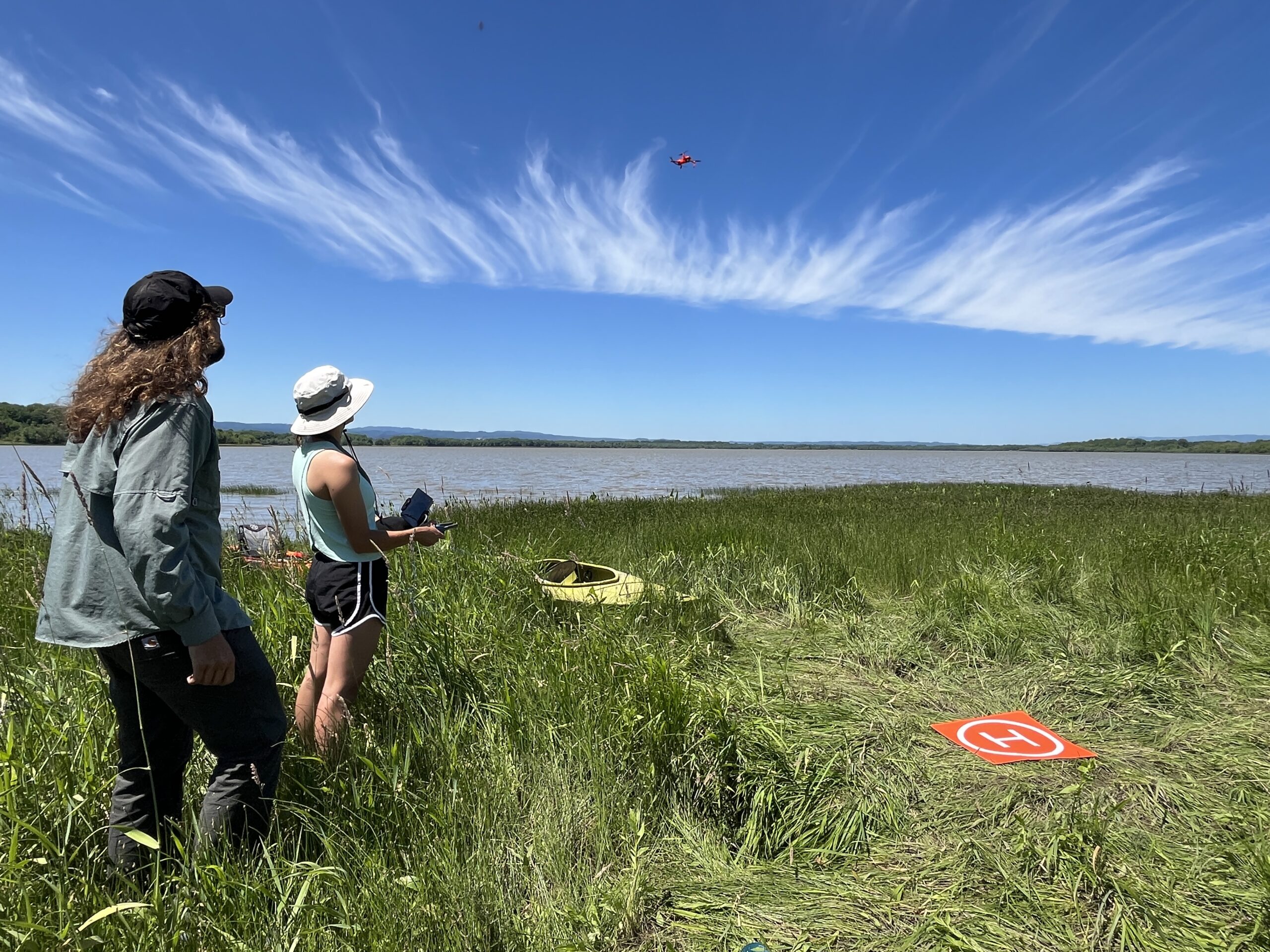 lake_drone two people looking at and flying a drone over a lake
