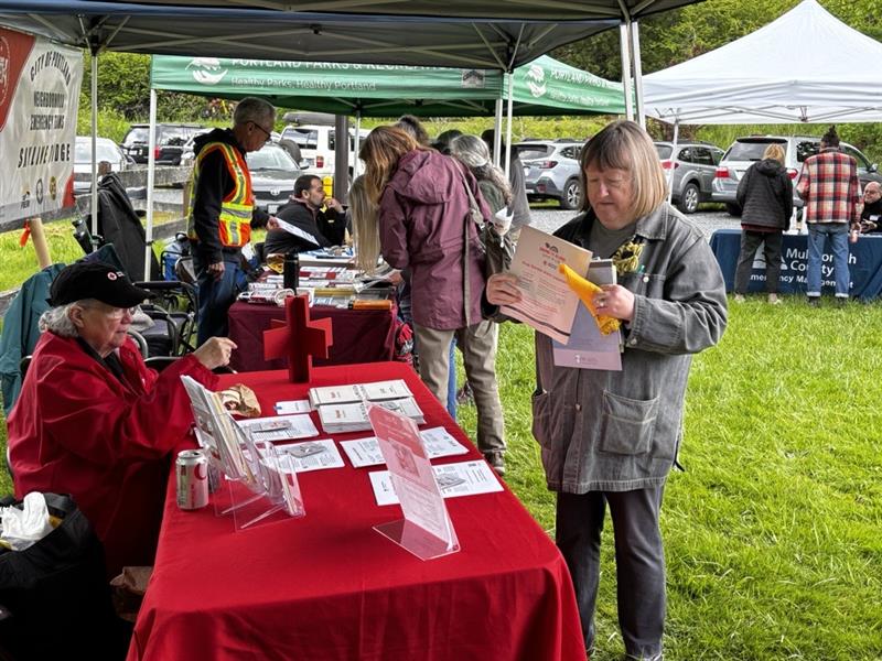 A woman sits at a table with a red tablecloth while another woman looks at a piece of paper in front of the table.