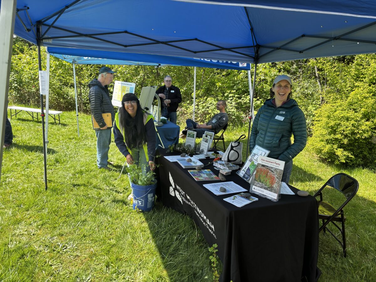 Two staff members smile next to a table at an outdoor event.