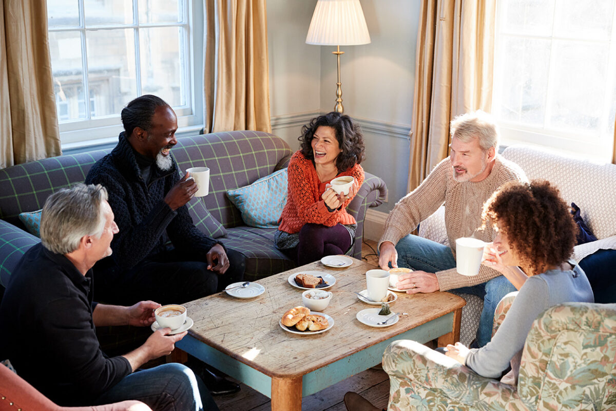 Group of men and women sitting on couches eating breakfast and laughing.