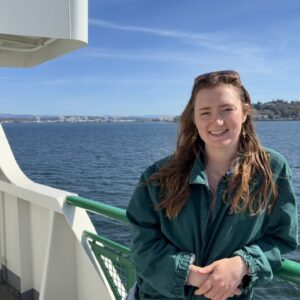 Gillian smiles at the camera on the deck of a ferry with water and an island in the background.