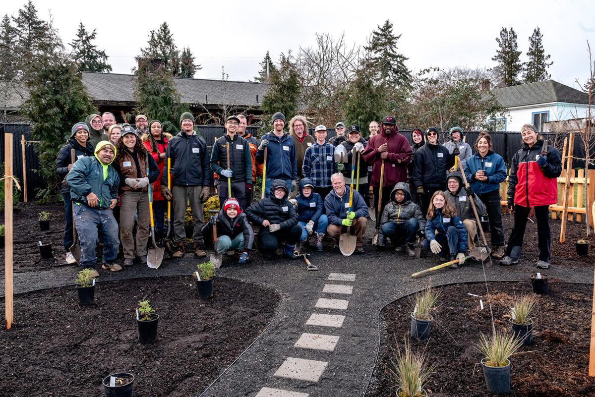 Group of people in jackets and holding shovels pose in a garden