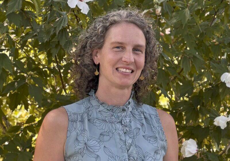 Casey, a white woman with curly gray hair, smiles and is wearing a blue floral shirt.