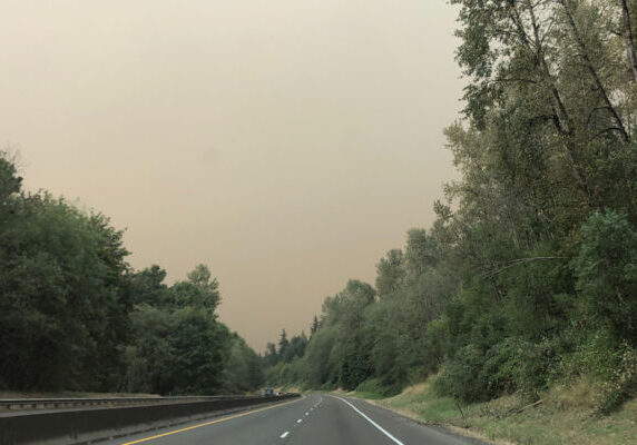 Highway with trees on side of road and brown smoke filling the sky