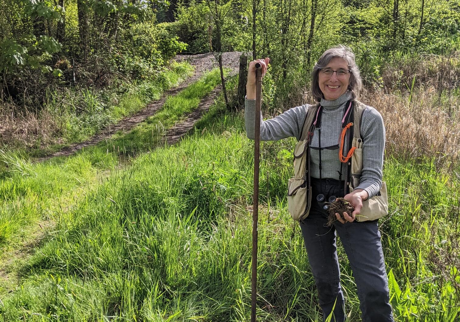 Our staff member Kammy smiles in a grassy area while leaning on a shovel