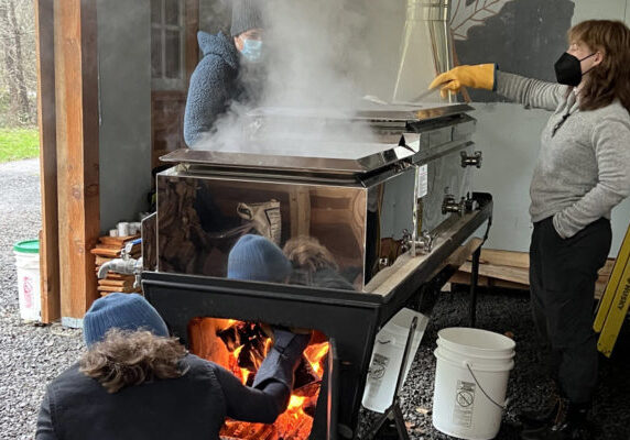 people tending a fire under a sap boiling vat