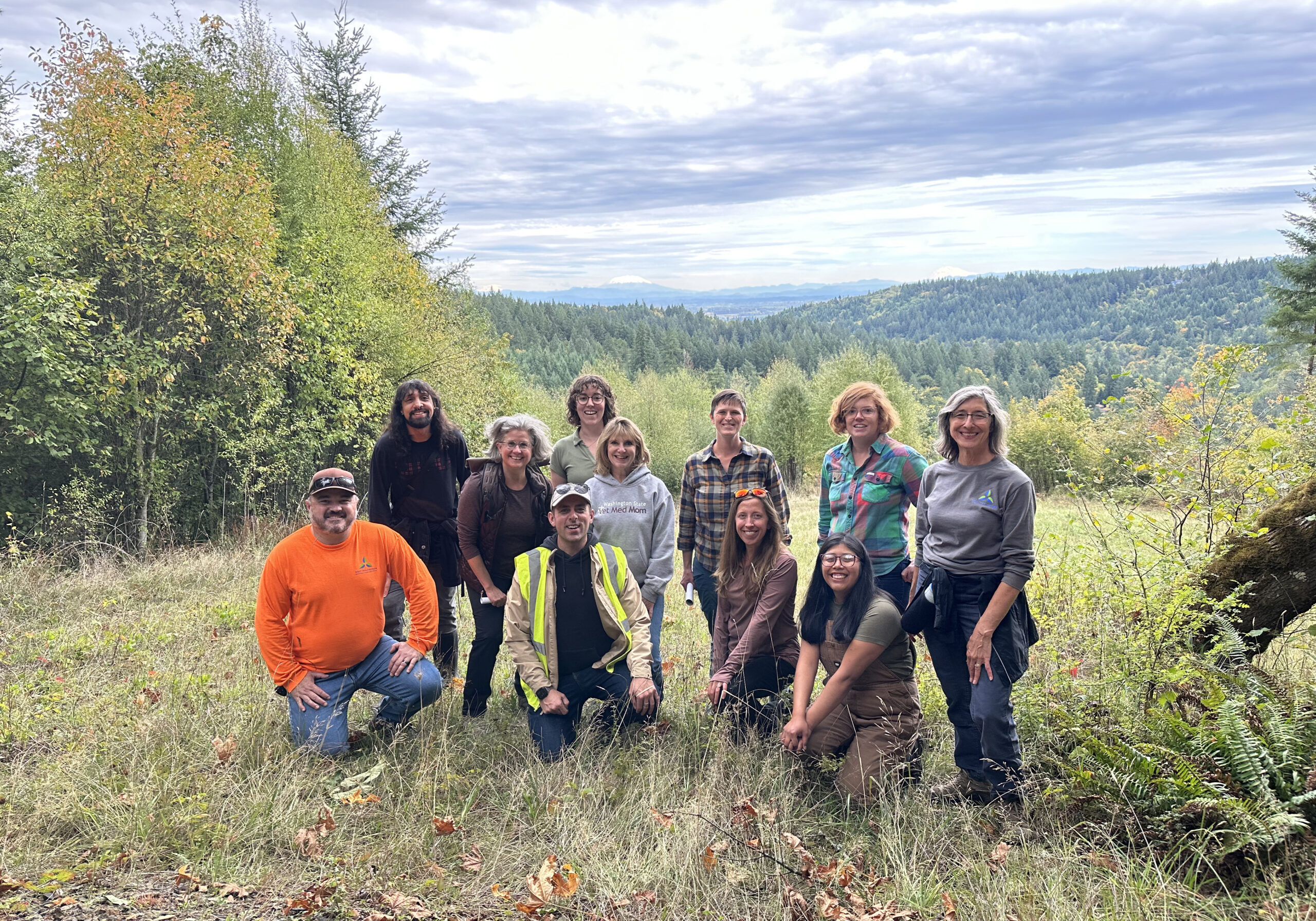 picture of the staff smiling on a hillside with a cloudy sky in the background