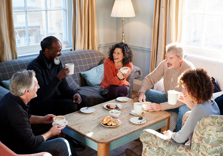 Group of men and women sitting on couches eating breakfast and laughing.