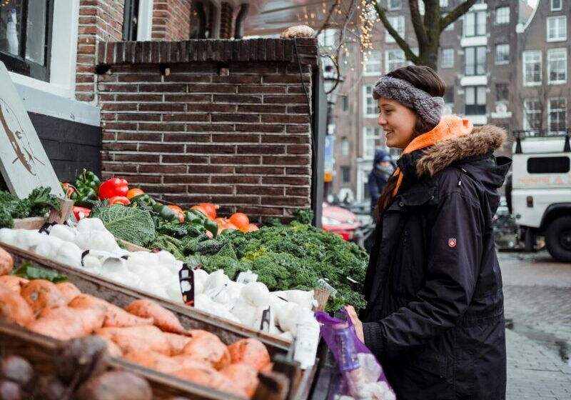 Woman with winter coat on looks at vegetables on a table, like at a farmer's market stand or shopping from Portland CSAs.