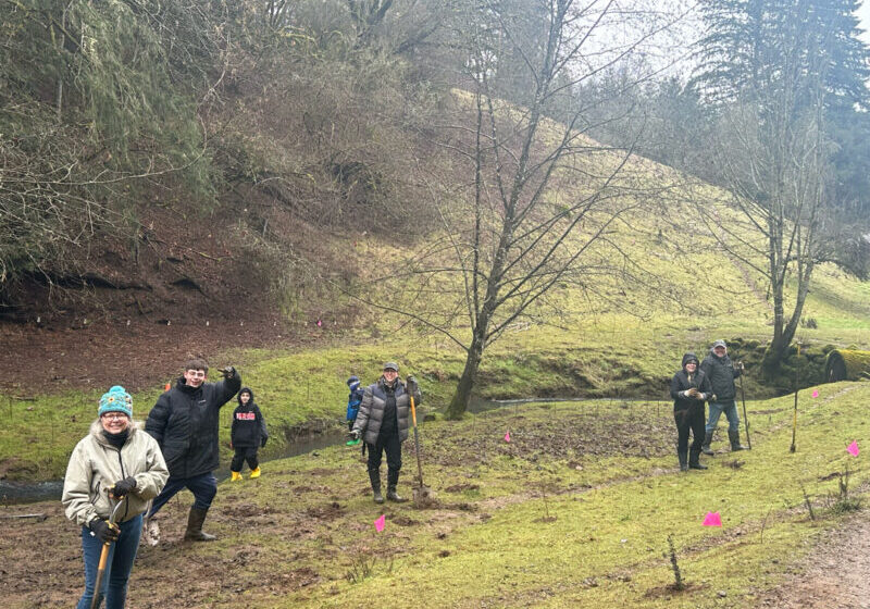 Volunteers smiling at the camera on a grassy, muddy hill on a rainy day